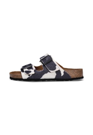 Sandale à motif vache noire et blanche avec deux brides réglables, semelle en liège et semelle noire, vue de profil sur fond blanc.