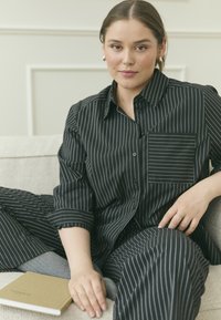 Black and white striped shirt and pants set, featuring a button-up design, pocket detail, and smooth fabric texture. Notebook on lap.