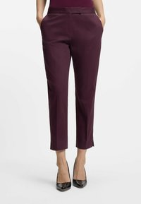 Burgundowe spodnie 3/4 z płaskim przodem, dwoma bocznymi kieszeniami i gładką teksturą. Połączone z czarnymi butami na wysokim obcasie, podkreślającymi nogawki.