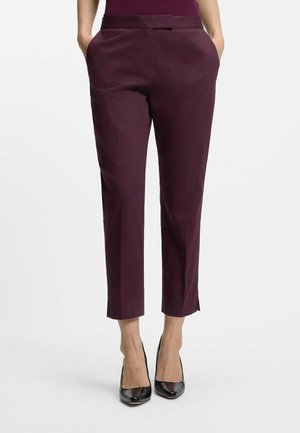 Celana cropped burgundy dengan bagian depan datar, dua saku samping, dan tekstur yang halus. Dipadukan dengan sepatu hak tinggi hitam, menonjolkan ujung celana.