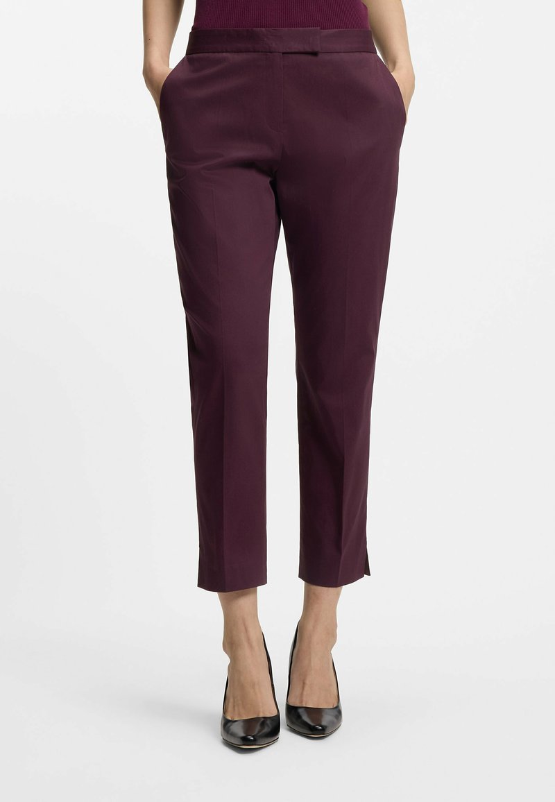 Burgundowe spodnie 3/4 z płaskim przodem, dwoma bocznymi kieszeniami i gładką teksturą. Połączone z czarnymi butami na wysokim obcasie, podkreślającymi nogawki.