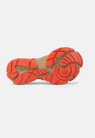 Kengän pohja, jossa on kirkkaan oranssi ja beige kumipinta, featuring uria pidon parantamiseksi ja ympyrälogo pohjassa.