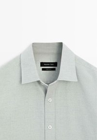 Camicia grigia chiaro con bottoni, colletto aperto, tessuto morbido e bottoni bianchi. Etichetta con scritto "Massimo Dutti." Design semplice e minimalista.
