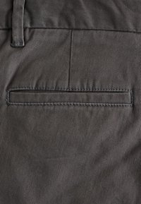 Grauer Stoff mit rippenartiger Textur, der eine flache Paspeltasche aufweist. Die Nähte sind tonal und der Stoff wirkt glatt und strapazierfähig.