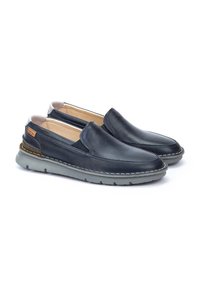 Zapatos slip-on de cuero en color navy con puntera redondeada, paneles laterales elásticos y suela de goma gris con detalles de costura blanca.