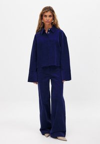 Navy corduroy two-piece set featuring a cropped shirt with a button closure and wide-leg pants. The fabric has vertical ribs and a soft texture.