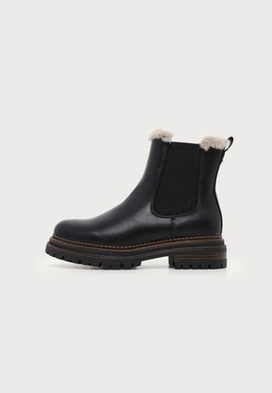 Μαύρο δερμάτινο μποτάκι με χοντρή σόλα, ελαστικό πλευρικό πάνελ και ανοιχτό γκρι γούνινη επένδυση στα πάνω άκρα, δείχνεται σε απλό φόντο.