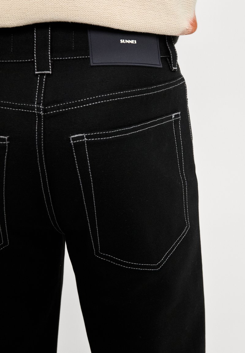Schwarze Denim-Jeans mit weißen Kontrastnähten; verfügen über zwei Gesäßtaschen und ein Markenlabel am Bund. Gerades Bein Design.