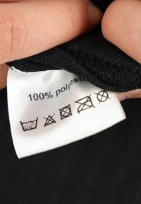 Sort stofetiket med plejeinstruktioner: 100% polyester, vask ved 60°C, ingen blegemiddel, ingen tørretumbler, stryg ikke, ingen kemisk rens.