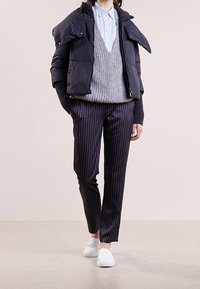Chaqueta de plumas en color marino con un alto cuello, suéter de punto gris, camisa azul claro, pantalones a rayas en color marino y zapatos slip-on blancos.
