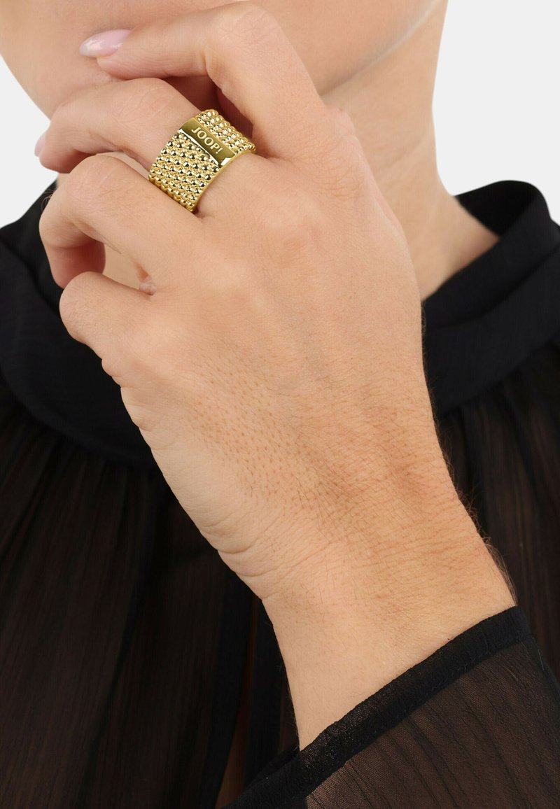 Anello in metallo color oro con design a rete testurizzata, dotato di una fascia liscia con l'iscrizione "JOOP!" su un lato.