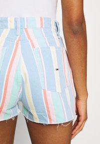 Pantalones cortos de mezclilla azul claro con rayas verticales en colores pastel. Incluyen dos bolsillos traseros y detalle de dobladillo deshilachado.