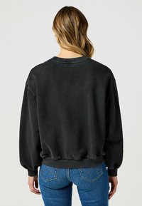 Czarna bluza z ribbowym okrągłym dekoltem i rękawami balonowymi, o fakturowanym wykończeniu. W zestawie z niebieskimi dżinsami.