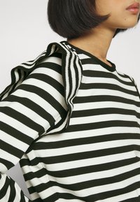 Maglione a righe verde scuro e bianco, con un accentuato volant lungo la cucitura della spalla, realizzato in un tessuto testurizzato.