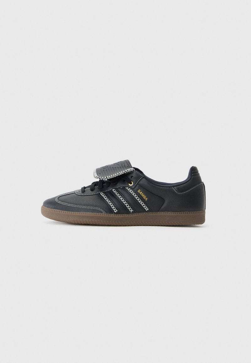 Svart lærsneaker med grå sømmer, tre hvite striper, en tekstury svart stropp og en brun gummisåle. "SAMBA" er trykt i gull.