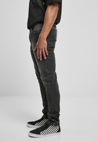 Pantalones vaqueros negros de corte slim, con un ligero desgaste; combinados con zapatillas altas a cuadros en blanco y negro.