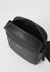 Sort crossbody taske med en glat læderoverdel og en mønstret syntetisk krop. Den har en lynlåslukning og en aftagelig rem.