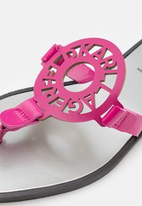 Vaaleanpunainen nahkasandaali, jossa on leikattu pyöreä emblem ja kontrastivärinen hopeinen sisäpohja, sekä tyylikäs musta ulkopohja ja säädettävät hihnat.