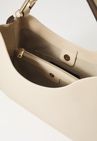 Šviesiai ruda odinė rankinė su lygiu paviršiumi, pasižyminti auksine užtrauktuku, vidine kišenėle ir magnetiniu spaustuku.