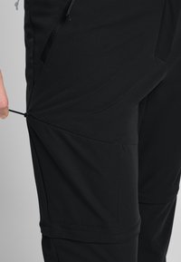Zwarte outdoorbroeken van een soepel, lichtgewicht materiaal. Kenmerken zijn onder andere een zijzak, verstelbare trekkoorden en geïnterpreteerde naden voor comfort.