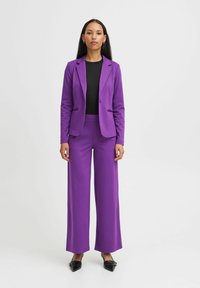 Blazer ajusté violet et pantalon à jambes larges, associé à un haut noir. Tissu lisse avec un design structuré, sans motifs ni accents visibles.