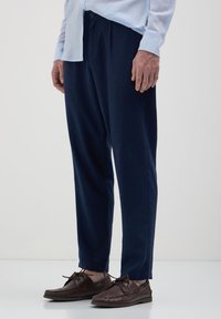 Pantaloni blu navy a taglio morbido realizzati in un tessuto soffice, caratterizzati da una texture liscia e un design a gamba dritta, abbinati a scarpe mocassino marroni.
