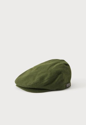 Casquette plate vert olive avec une petite étiquette en tissu sur le côté, présentée sur un fond clair uni.
