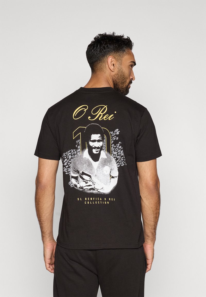 Camiseta negra con un gráfico impreso de un jugador con el texto "O Rei" y "10" en dorado y blanco, con un fondo de diseño texturizado.
