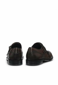 Paar dunkelbraune Lederschnürschuhe mit doppelten Monk-Strap-Schnallen, von hinten auf weißem Hintergrund gezeigt.