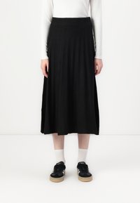 Svart, kne-lengde, plissert skjørt laget av et teksturert stoff, sammen med svarte sneakers og hvite ankelstrømper.