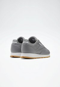 Harmaat urheilukengät, joissa on sileä nahkapäällinen, pehmustettu kaulus ja valkoinen välipohja. Varustettu kumipohjalla ja kantapään brändäysyksityiskohdalla.