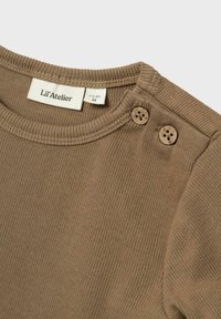 Top in maglia a coste marrone con scollo rotondo e due bottoni decorativi sulla spalla. L'etichetta interna mostra le informazioni relative alla taglia.