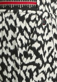 Mustekki ja valkoinen kuviollinen kangas, jossa on abstrakti muotoilu. Sisältää punaruudullisen yksityiskohdan ja mustan brändätyn napin. Teksturoitu puuvillakangas.