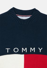 Strickpullover in Marineblau mit roten und weißen geometrischen Mustern. Verfügt über einen Rundhalsausschnitt und "TOMMY" in weißen Buchstaben auf der Brust.