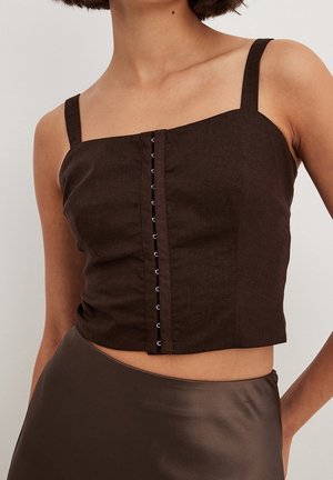 Débardeur court marron avec fermetures à agrafes à l'avant, porté avec une jupe en satin marron foncé sur une personne.