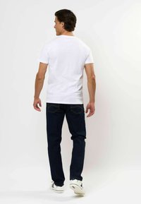 Biała koszulka z krótkim rękawem w połączeniu z ciemnoniebieskimi dżinsami, prezentująca klasyczny krój i minimalistyczny design. Podkreślona jasnym przeszyciem.