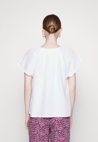 Top branco de mangas curtas com um corte solto, tecido texturizado e detalhe nas costas com franzido, combinado com calças rosas estampadas.