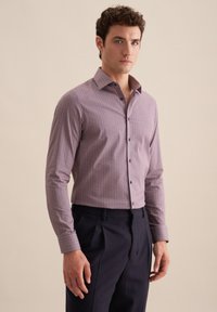 Koszula z długim rękawem w fioletowym materiale z geometrycznym wzorem, z kołnierzykiem zapinanym na guziki i guzikiem z przodu, w połączeniu z ciemnymi spodniami.