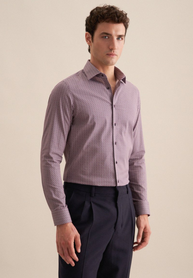 Koszula z długim rękawem w fioletowym materiale z geometrycznym wzorem, z kołnierzykiem zapinanym na guziki i guzikiem z przodu, w połączeniu z ciemnymi spodniami.