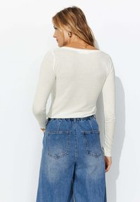 Haut à manches longues crème avec un dos dégagé, associé à un jean en denim bleu taille haute à coupe ample avec deux poches arrière.