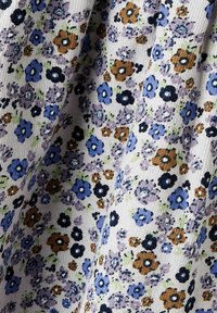 Blomstret stoff med små blå, lilla og brune blomster på hvit bakgrunn; har en teksturert vev og varierende blomsterstørrelser.