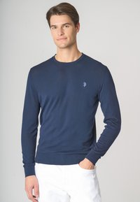 Maglione a maniche lunghe blu navy con scollo rotondo, realizzato in materiale morbido, con colletto e polsini a coste, e un discreto logo ricamato sul petto.