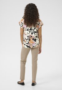 Cvetlični vzorec na majici s kratkimi rokavi v črni, roza in krem barvi; kombinirana z bež oprijetimi hlačami in črnimi balerinkami.