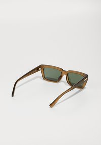 Occhiali da sole color marrone con lenti verdi rettangolari, montatura spessa e aste diritte. Presentano dettagli decorativi e incisione del marchio.