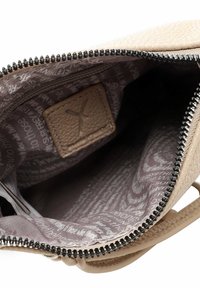 Interno di una borsa a tracolla in pelle beige Tessurato, con chiusura a zip e foderatura a motivo marrone chiaro con testo bianco.