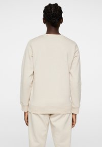 Beige sweatshirt met lange mouwen en geribbelde manchetten, met een ronde halslijn en een soepele textuur, van achteren weergegeven.