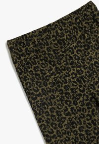 Leggings negros con un patrón de estampado de leopardo en verde oscuro y hilos dorados. Cintura elástica suave con tejido texturizado.