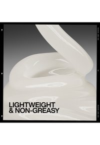 Crema bianca lucida che viene mescolata, evidenziando una texture leggera e non grassa su uno sfondo sfumato grigio.