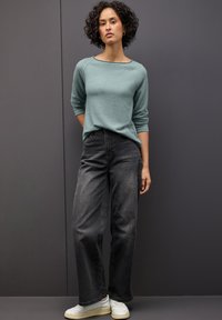 Maglione turchese chiaro con maniche a tre quarti, abbinato a jeans grigi scuri a vita alta e sneakers bianche. Stile semplice e vestibilità rilassata.