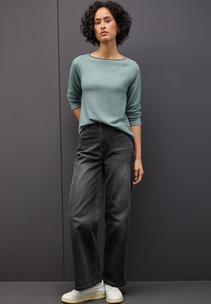Maglione turchese chiaro con maniche a tre quarti, abbinato a jeans grigi scuri a vita alta e sneakers bianche. Stile semplice e vestibilità rilassata.